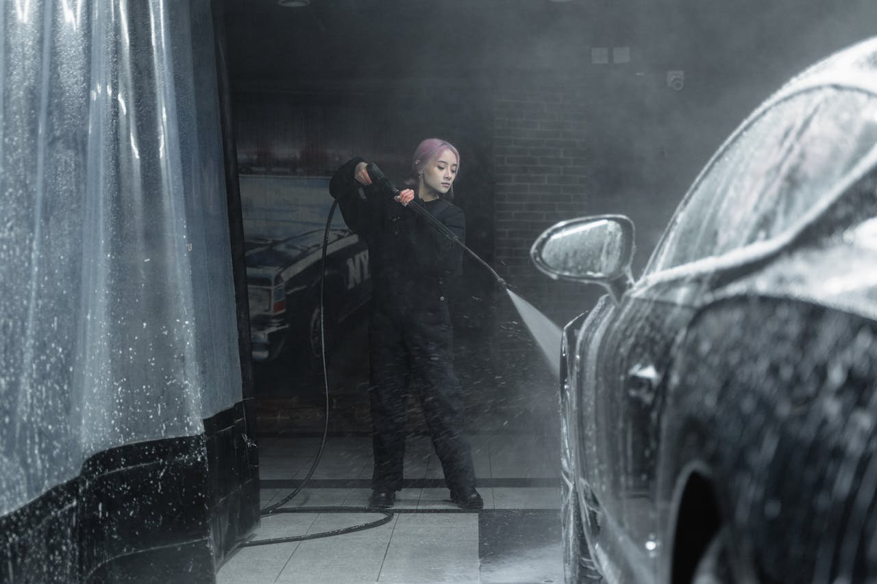 Mastering the First Impression: Your intriguing post title goes here A young woman in a black outfit washing a car with foam and water spray indoors.